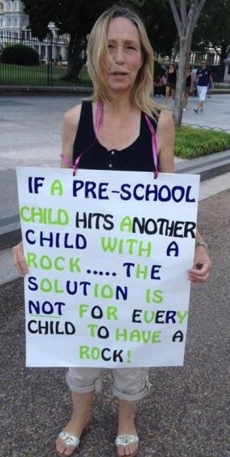 Woman with sign:  If a child hits another child with a rock, the solution is not for every child to have a rock.